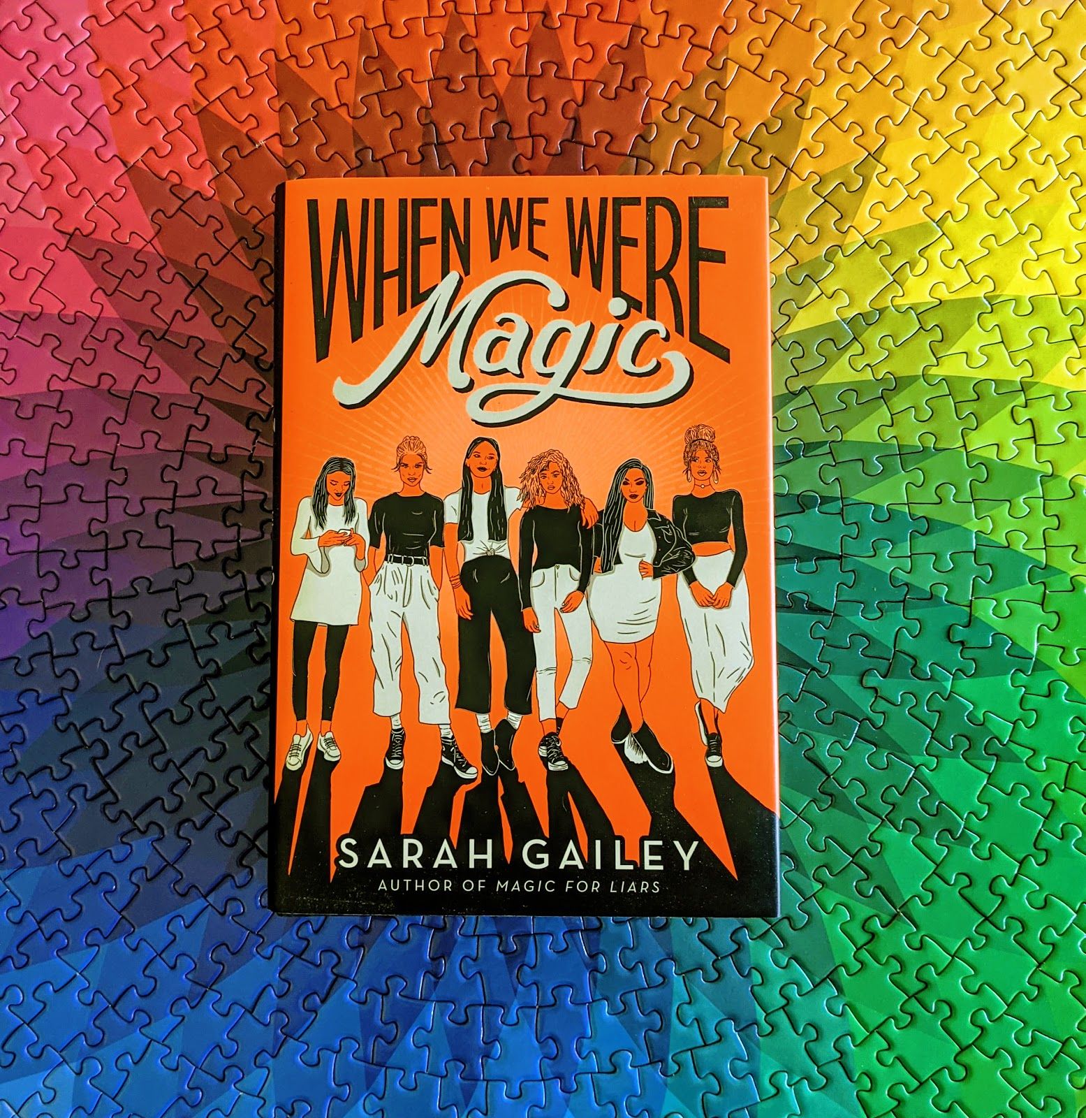 When We Were Magic has a bright orange cover featuring six femmes in black-and-white clothes looking like they don't give a shit about anyone else but each other. Here, the book is shown resting on a puzzle that is a rainbow spirograph. That puzzle took me a super long time to finish. I'm real proud of it.