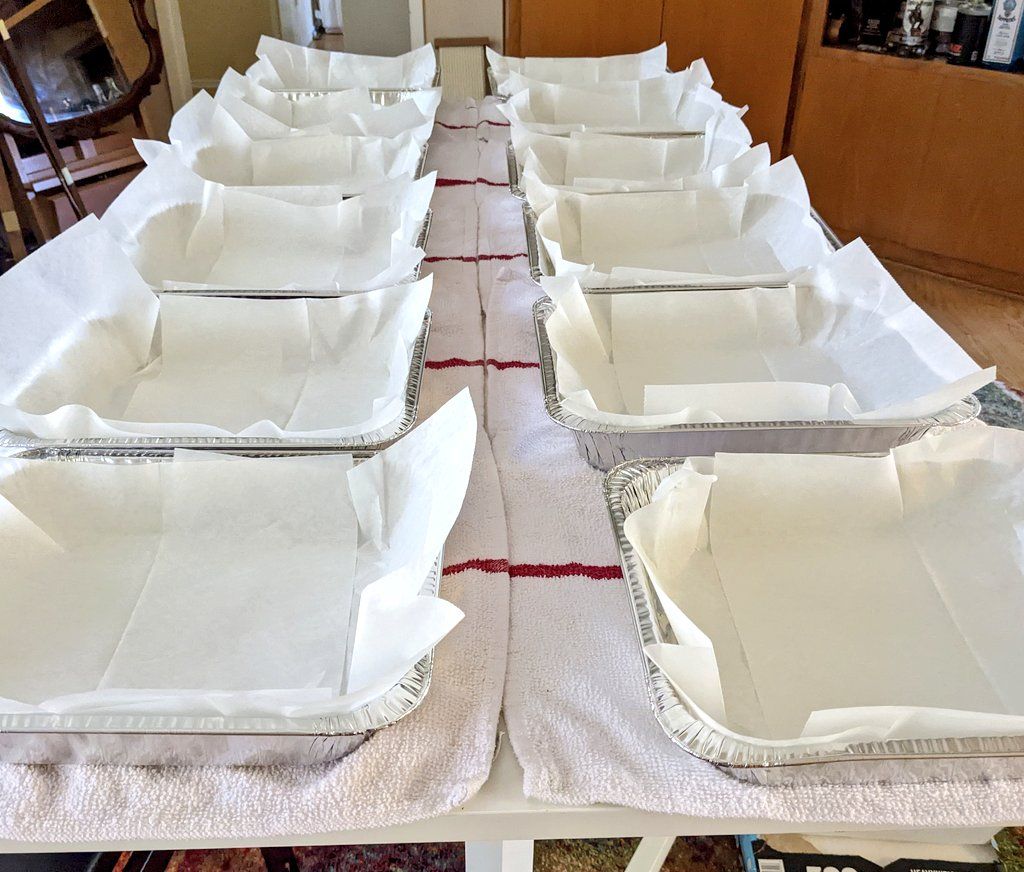 12 empty tin baking sheets lined up on a long table.