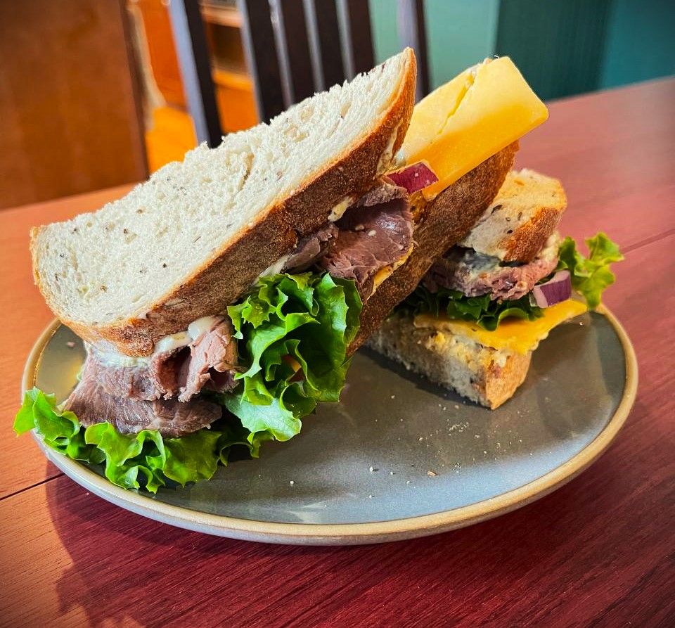 A grocery store roast beef sandwich, cut diagonally and stacked slantwise on a gray plate. A sprinklilng of crumbs on the plate tempt you.