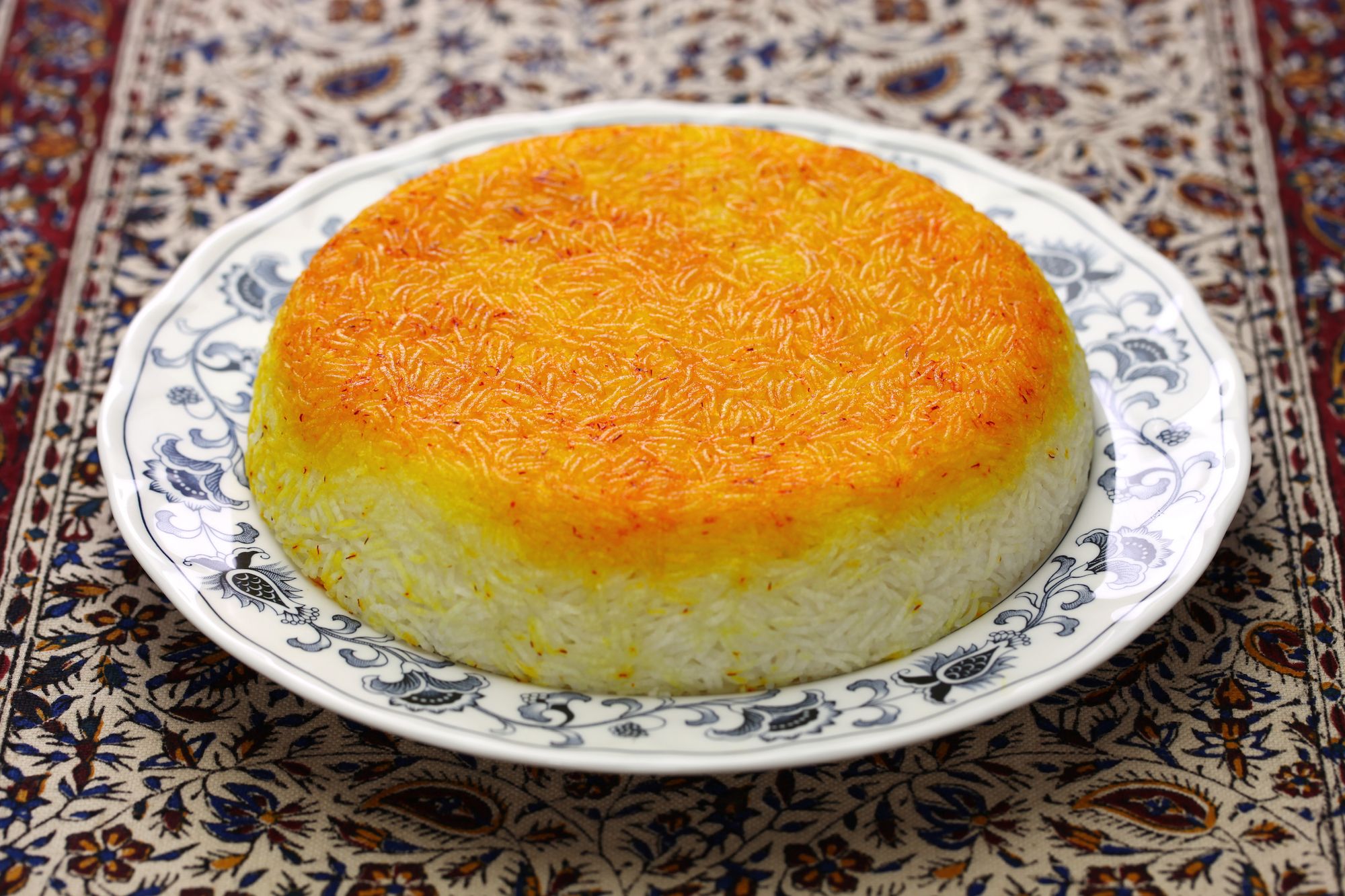 Tahdig rice on a white plate sitting in the center of a floral print table cloth.