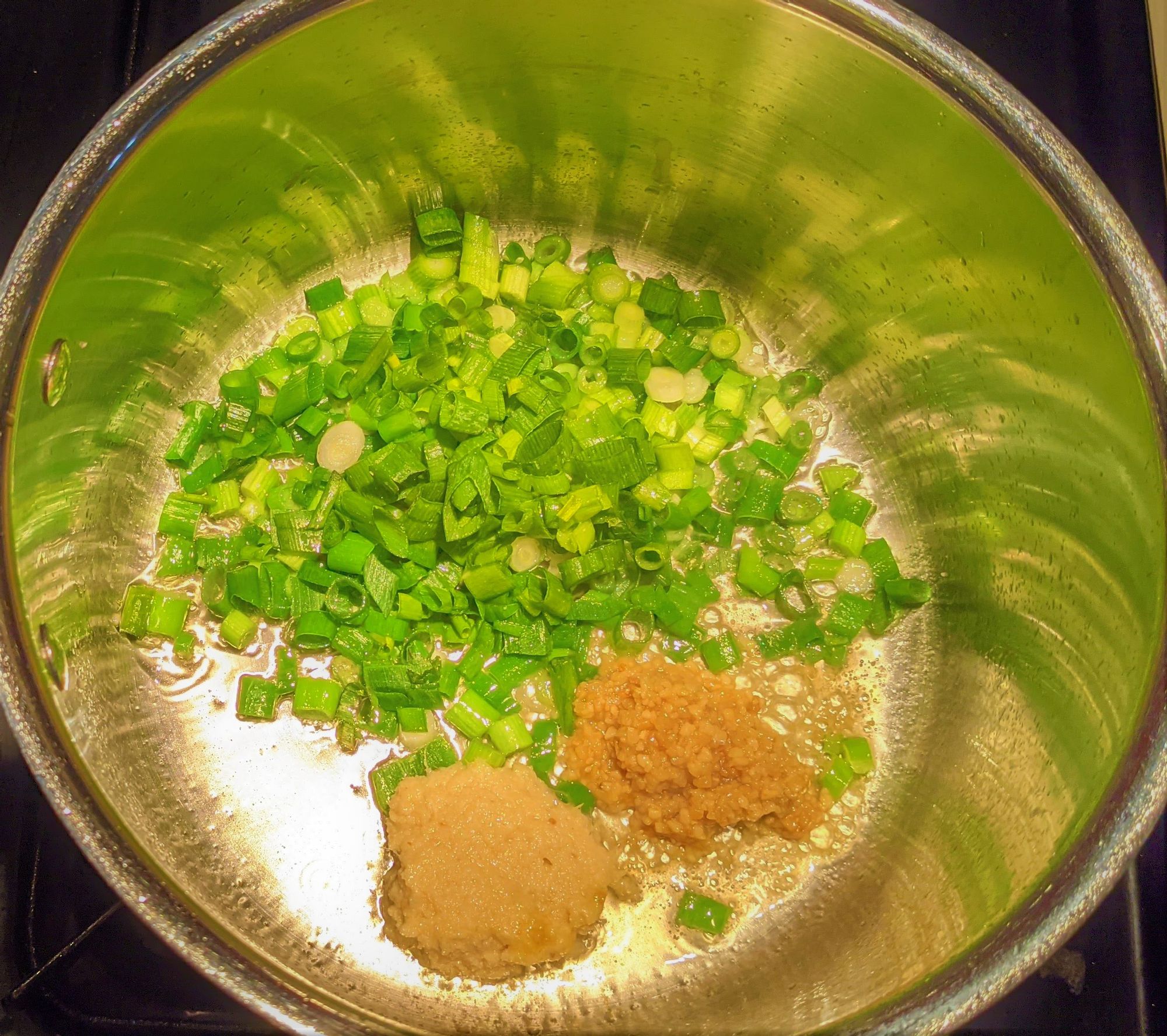 A pot with chopped green onions and two big spoonfuls of ginger and garlic paste.