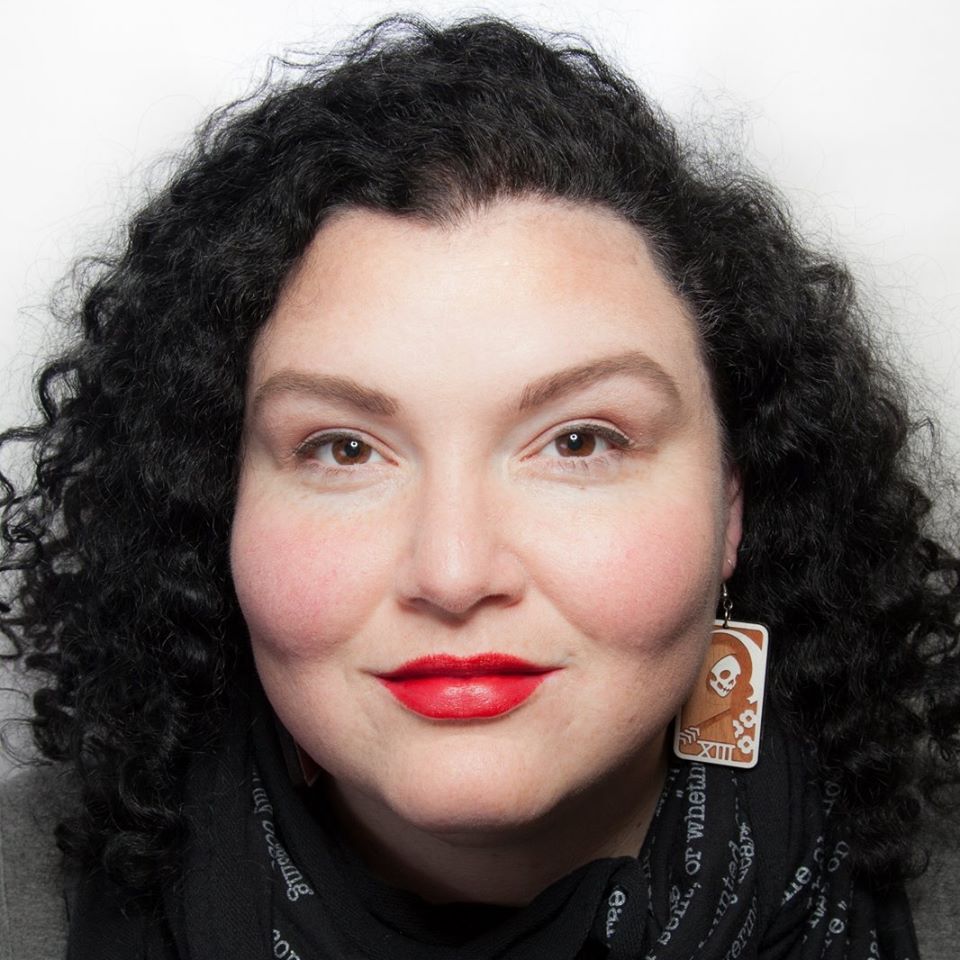 Portrait of Meg Elison, a fat femme with a full head of dark curls, warm, glinting brown eyes, and bright red lipstick.