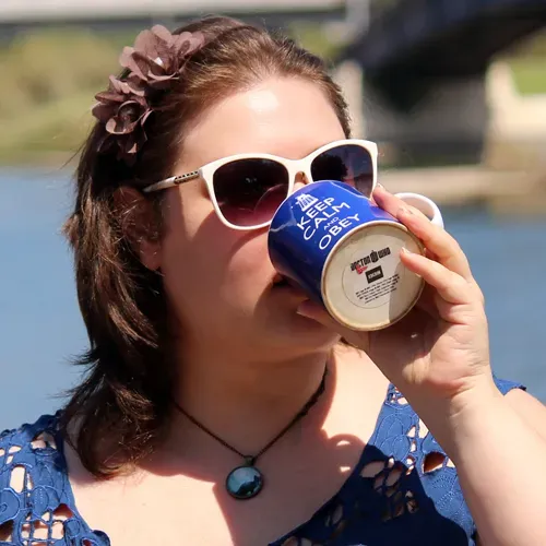Marina Berlin, a white woman with brown hair and sunglasses drinking from a blue mug that reads keep calm and obey