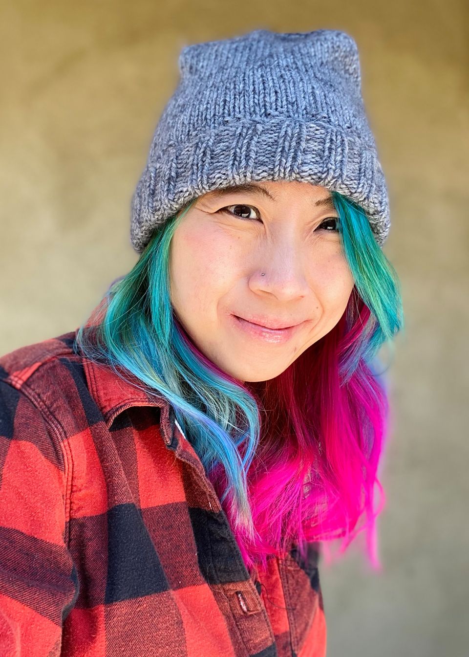 A Chinese-American person with brightly colored pink and blue hair, smirking goofily at the camera.