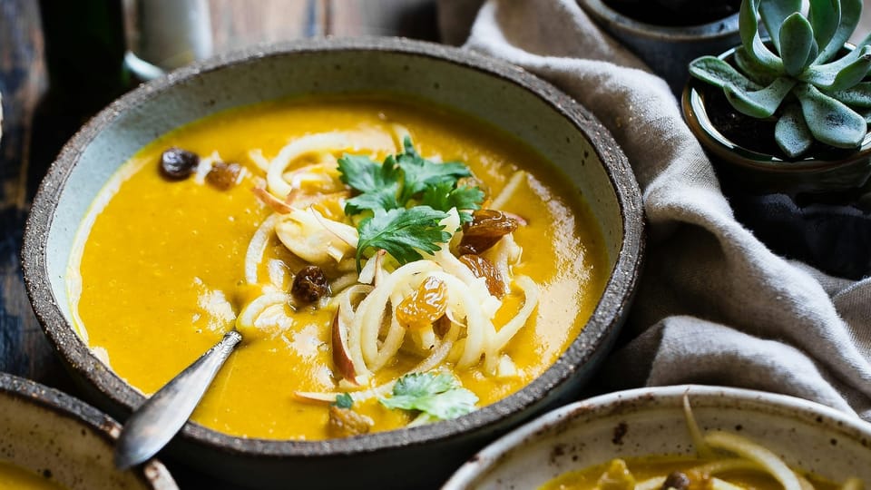 three bowls of creamy golden soup topped with raisins, onion, and parsley, served in earthenware bowls with spoons